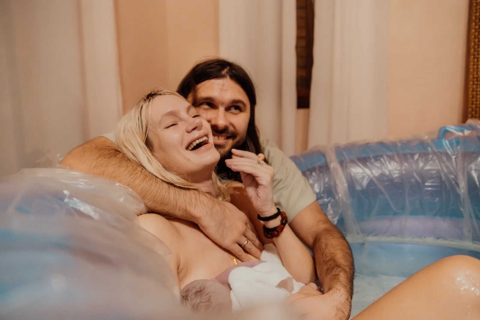 Casal sorrindo junto com o bebê logo após o nascimento em parto domiciliar