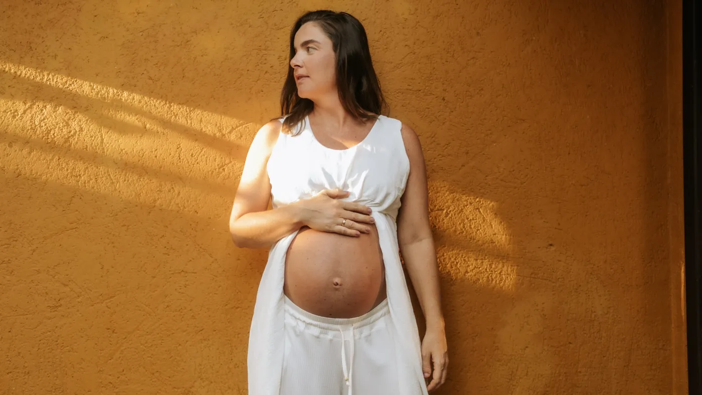 Gestante de branco diante de uma parede dourada
