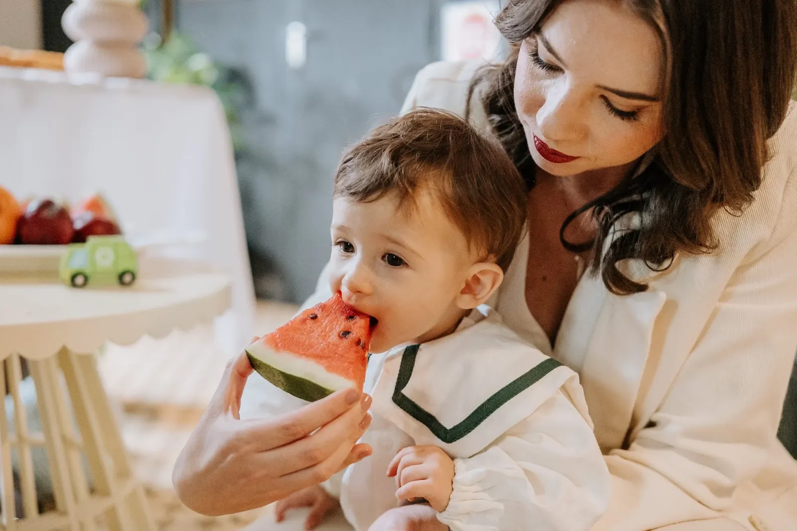 Bebê come melancia no colo da mãe