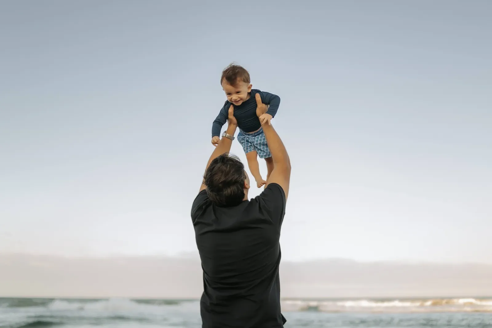 Pai ergue o bebê contra o céu na praia