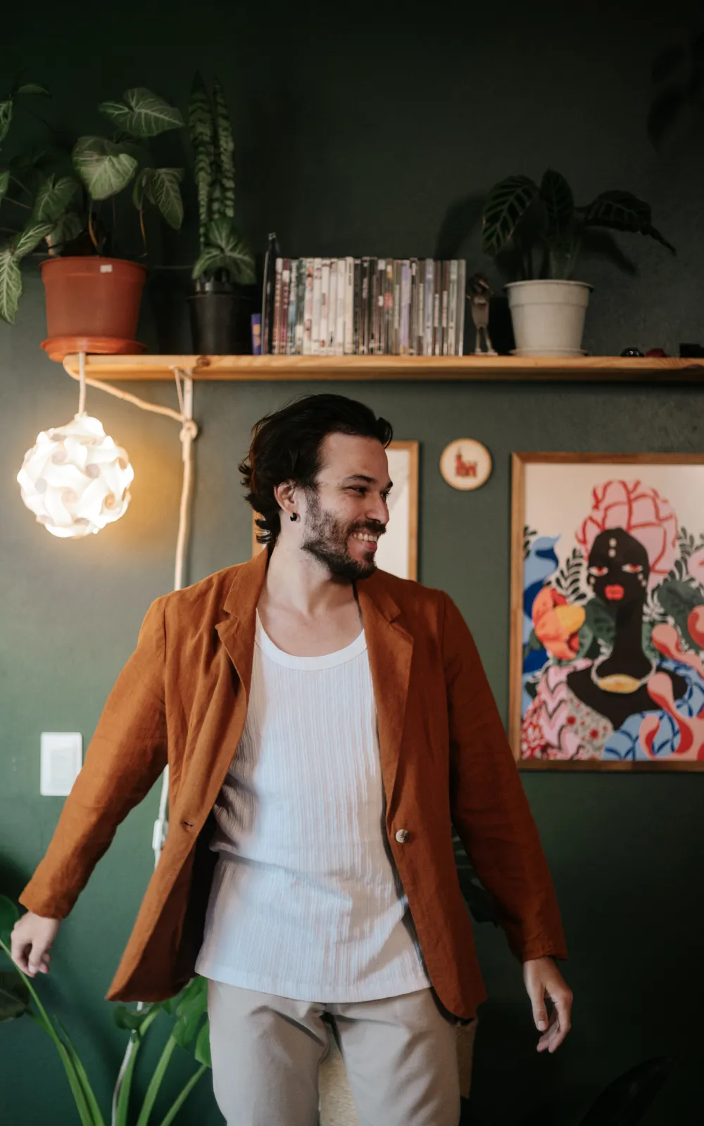 Homem de blazer caramelo sorrindo num ambiente com plantas